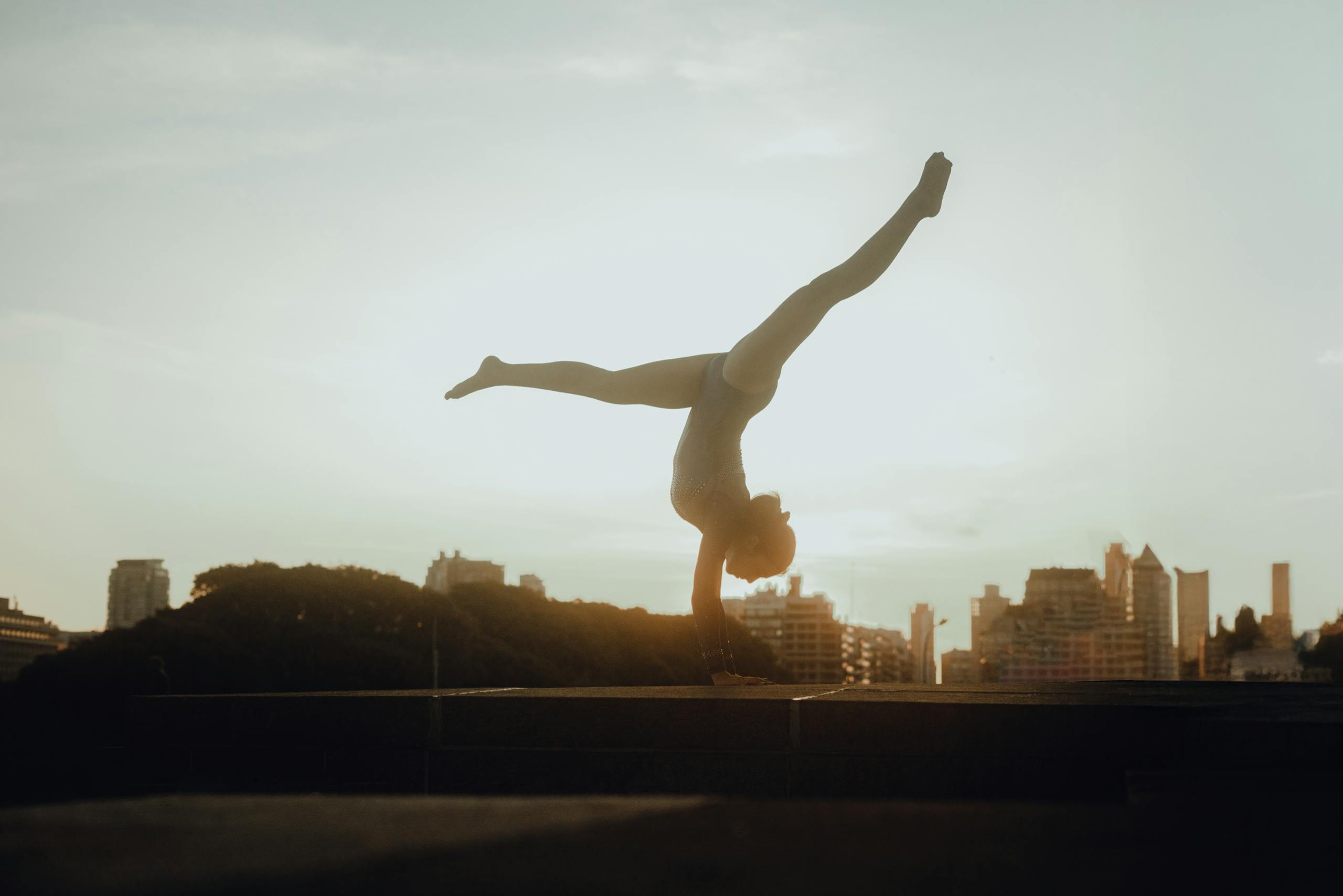 A gymnast performs an impressive handstand against the stunning skyline of Buenos Aires at sunset.
