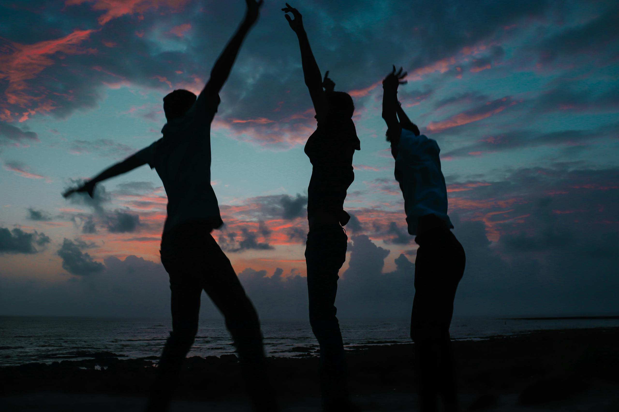 Silhouettes of three people dancing joyfully against a vibrant beach sunset sky.